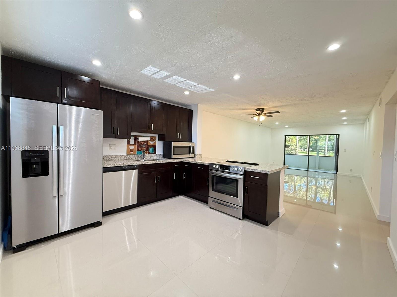 A kitchen with dark wood cabinets, stainless steel appliances, and light tile flooring — 6095 N Sabal Palm Blvd # 103, Tamarac FL 33319, TAMARAC, FL