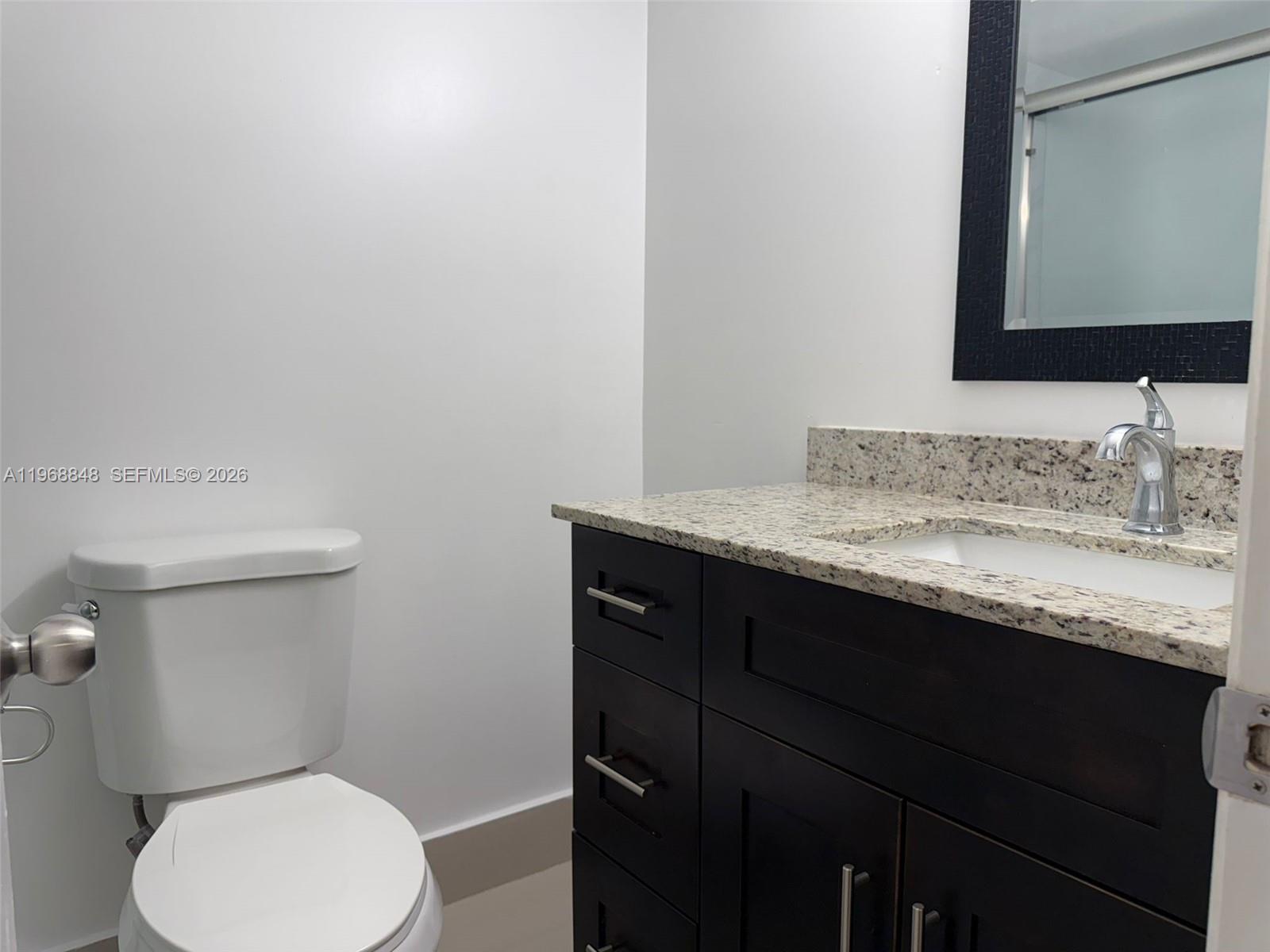 A bathroom features a dark wood vanity with a granite countertop and a white toilet — 6095 N Sabal Palm Blvd # 103, Tamarac FL 33319, TAMARAC, FL