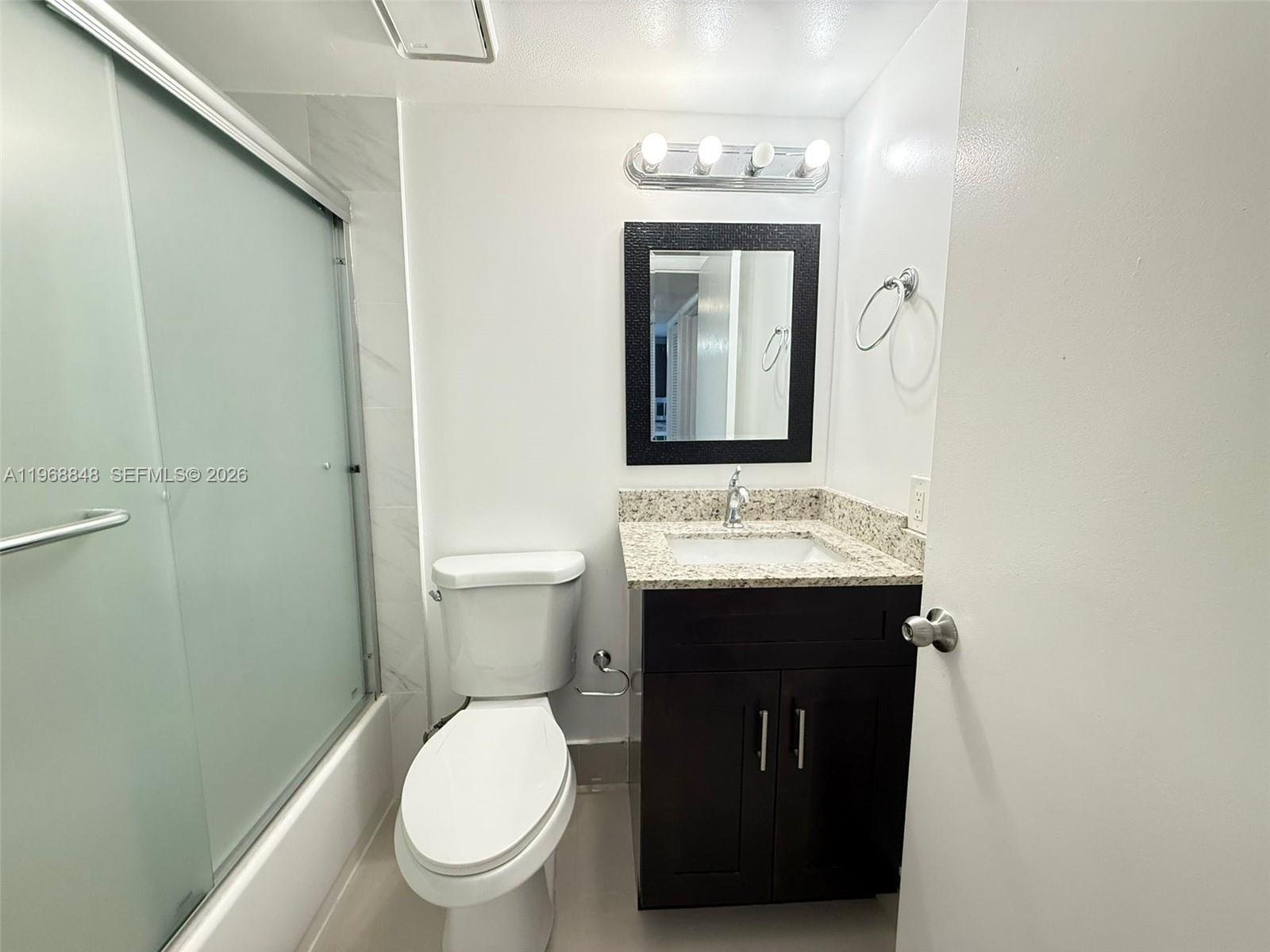 A bathroom features a dark vanity, granite countertop, toilet, and a glass-enclosed shower — 6095 N Sabal Palm Blvd # 103, Tamarac FL 33319, TAMARAC, FL