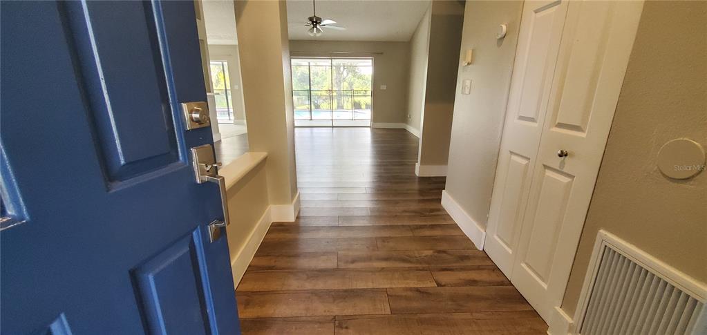 An entryway with wood-look flooring leads to a living area with a sliding glass door — 11608 WELLMAN DRIVE, RIVERVIEW, FL