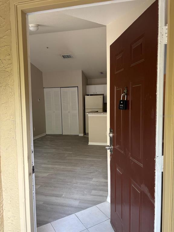 An open door reveals a living area with light wood-look flooring and a kitchen beyond — 6336 RALEIGH STREET UNIT 1215, ORLANDO, FL