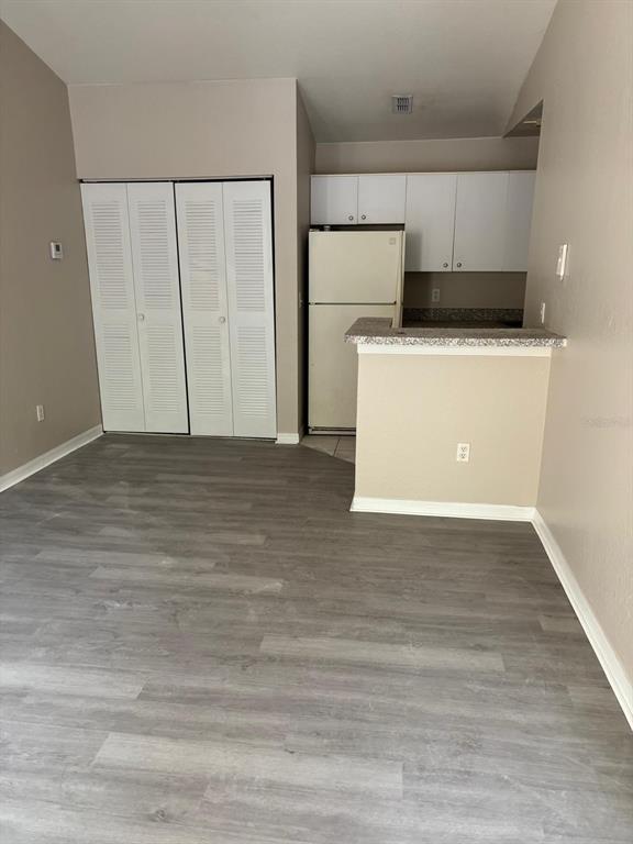A room with gray wood-look flooring, a white louvered closet, and an open kitchen area — 6336 RALEIGH STREET UNIT 1215, ORLANDO, FL