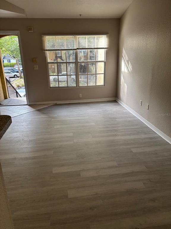 An empty living room features light-colored wood-look flooring, a large window, and an exterior doorway — 6336 RALEIGH STREET UNIT 1215, ORLANDO, FL