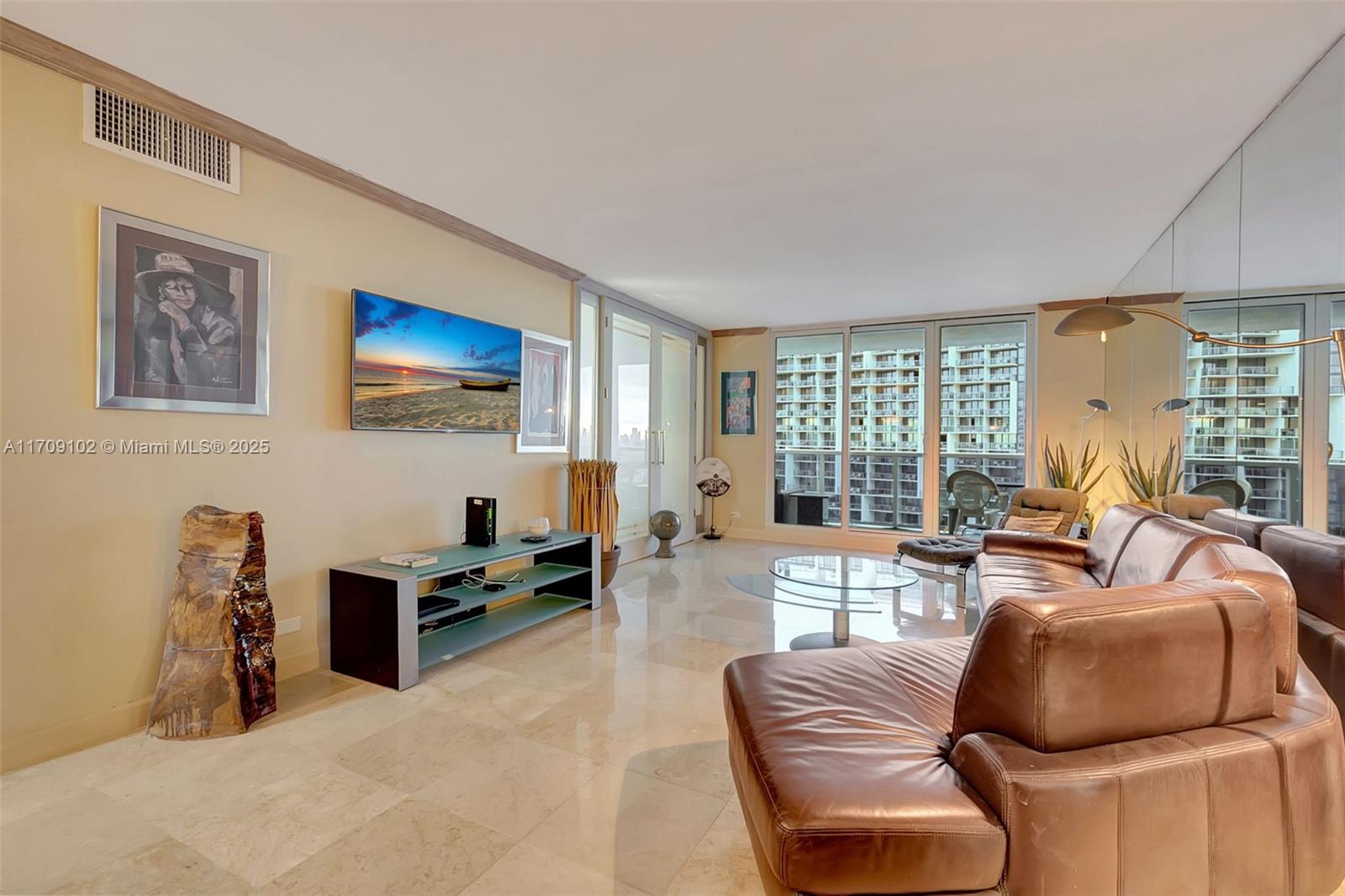 A living room features a brown leather sofa, a glass coffee table, and a wall-mounted television — 2301 Collins Ave # 1206, Miami Beach FL 33139, MIAMI BEACH, FL