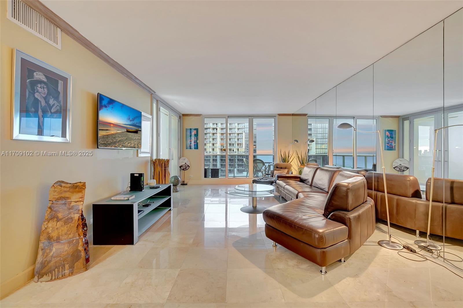 A living room features a brown leather sectional, glass coffee table, and a mirrored wall — 2301 Collins Ave # 1206, Miami Beach FL 33139, MIAMI BEACH, FL