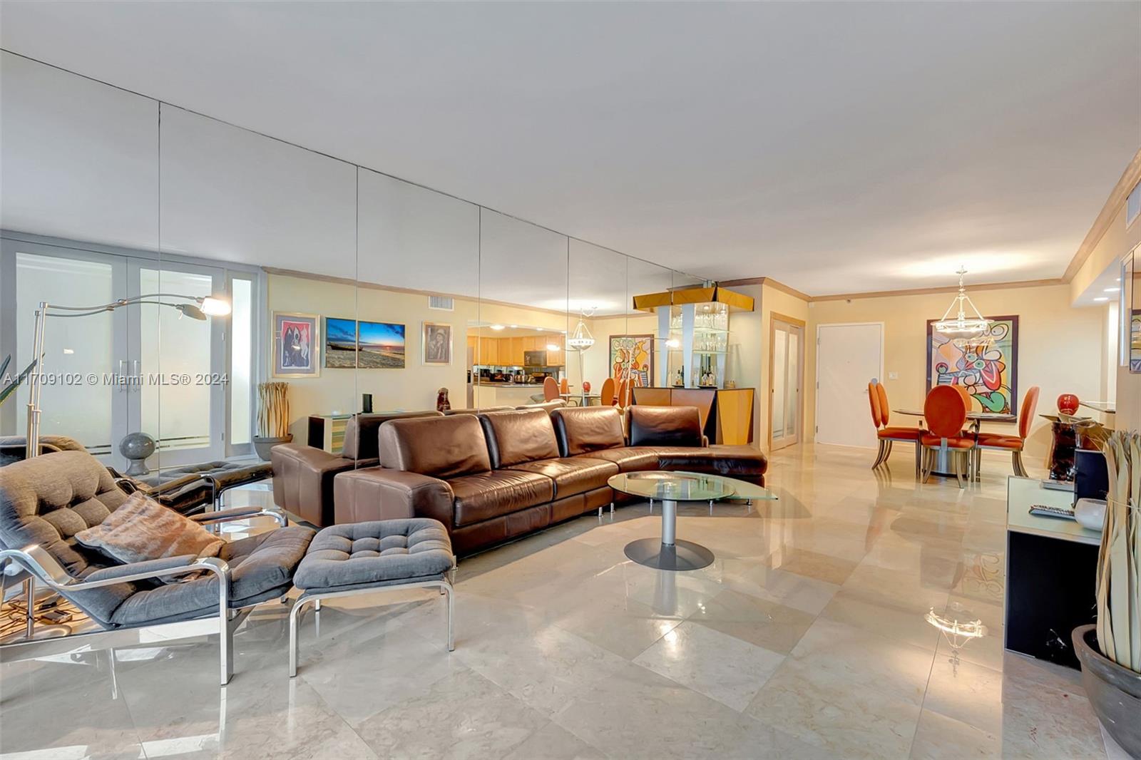 A living room features a large brown leather sectional, tiled floors, and a mirrored wall — 2301 Collins Ave # 1206, Miami Beach FL 33139, MIAMI BEACH, FL