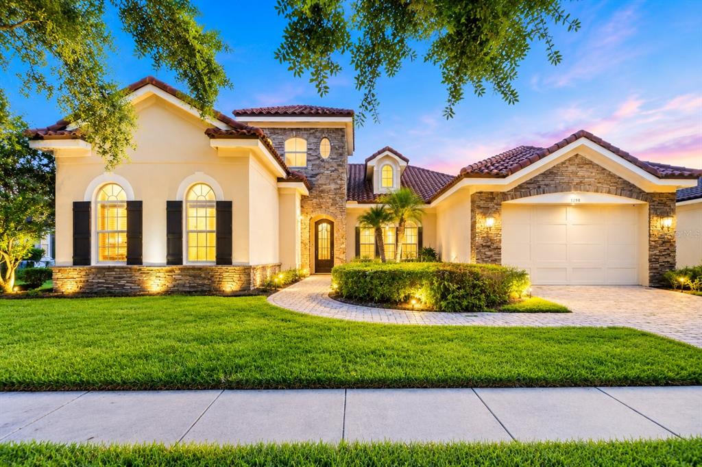A single-story house with a stone facade, tile roof, and a paved driveway at dusk — 1298 BELLA VISTA CIRCLE, LONGWOOD, FL