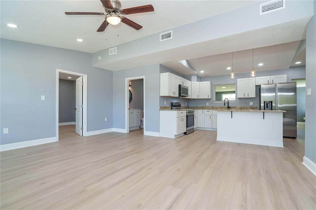 A bright, open-concept kitchen and living area featuring light wood flooring and white cabinetry — 9080 GRIGGS ROAD, ENGLEWOOD, FL