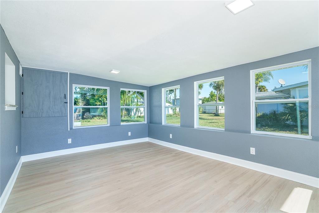 An empty room with blue walls, light wood-look flooring, and multiple windows — 9080 GRIGGS ROAD, ENGLEWOOD, FL