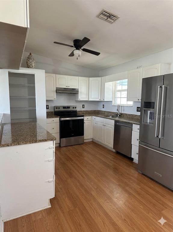 A kitchen features white cabinets, stainless steel appliances, granite countertops, and wood-look flooring — 900 NE 18TH TERRACE, CAPE CORAL, FL