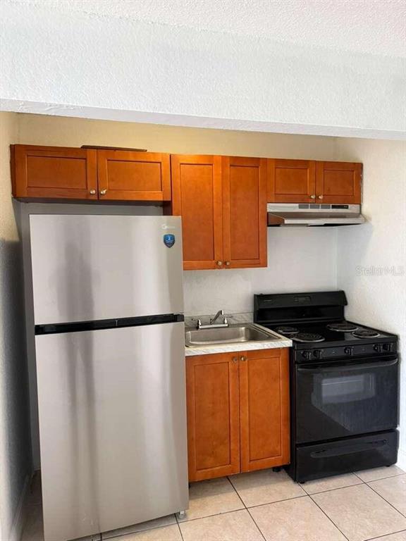 A small kitchen features stainless steel appliances, wood cabinets, and a black electric stove — 4251 NW 5TH STREET UNIT 121, FORT LAUDERDALE, FL