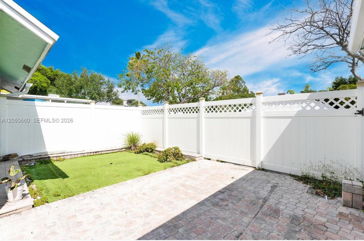 A small backyard features a paved patio, a patch of artificial turf, and white fencing — BOCA RATON, FL