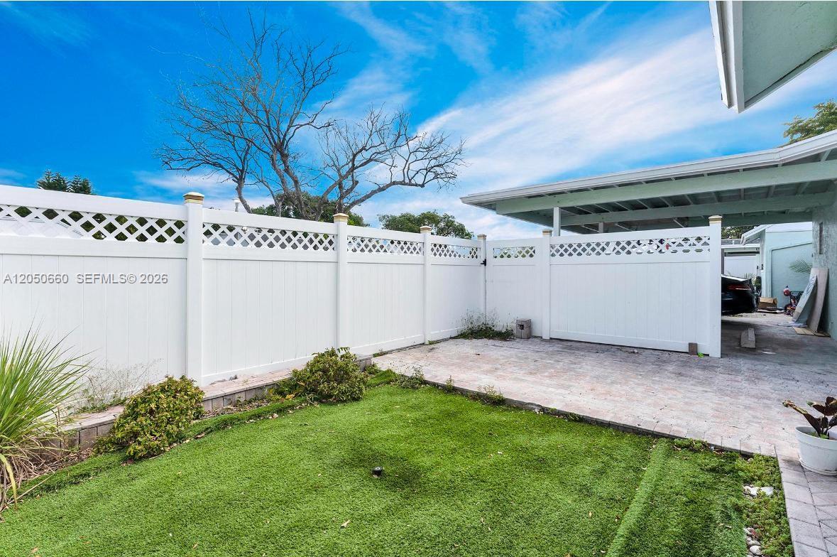 A fenced backyard features a paved patio area, a patch of grass, and a carport — BOCA RATON, FL