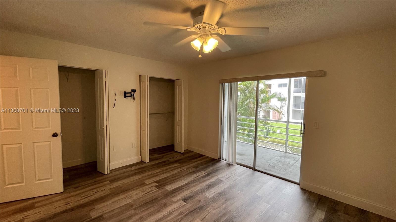 A bedroom features wood-look flooring, a ceiling fan, two closets, and a sliding glass door — 2878 Donnelly Drive # 204, Atlantis FL 33462, ATLANTIS, FL
