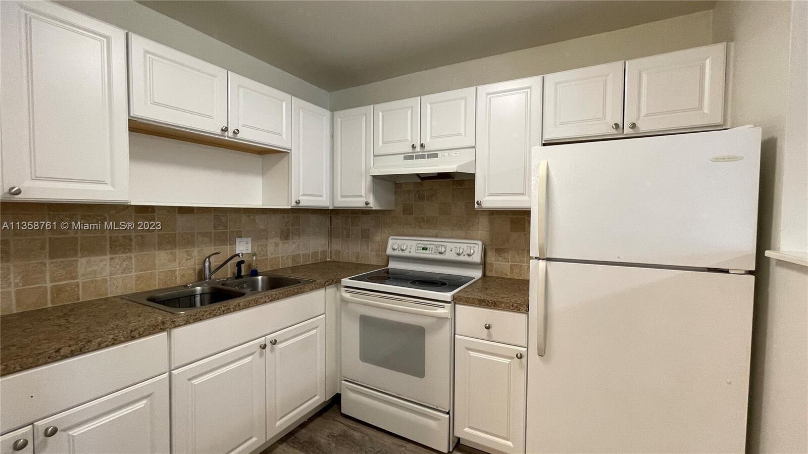 A kitchen features white cabinets, a white stove, a white refrigerator, and tan tile backsplash — 2878 Donnelly Drive # 204, Atlantis FL 33462, ATLANTIS, FL