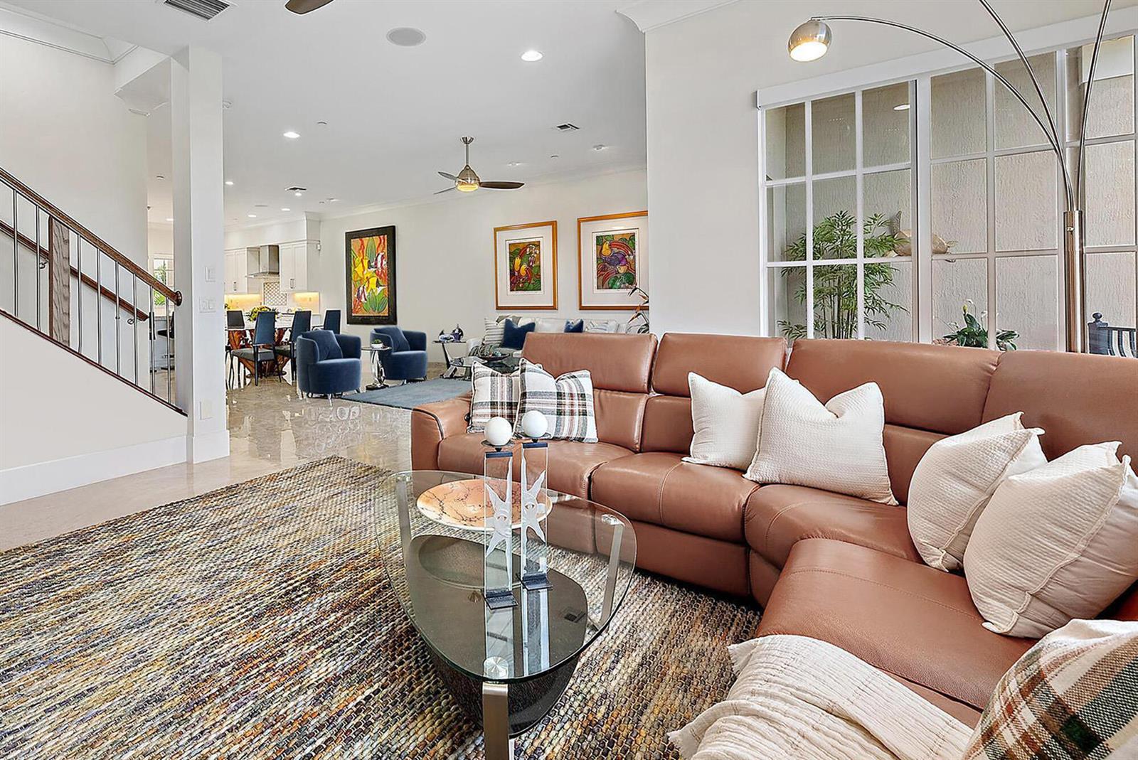 A living room features a brown leather sectional, a glass coffee table, and a staircase — 138 Tierra Lane # 6, Jupiter FL 33477, JUPITER, FL