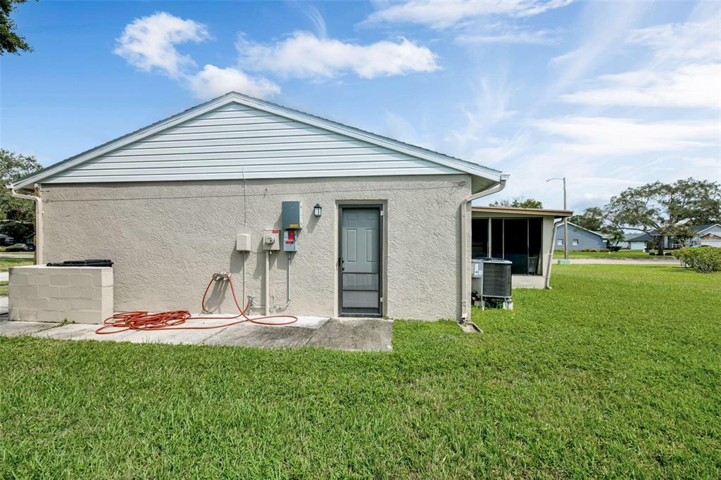 The exterior of a house features a stucco wall, a side door, and utility equipment — 3900 105TH AVENUE N, CLEARWATER, FL