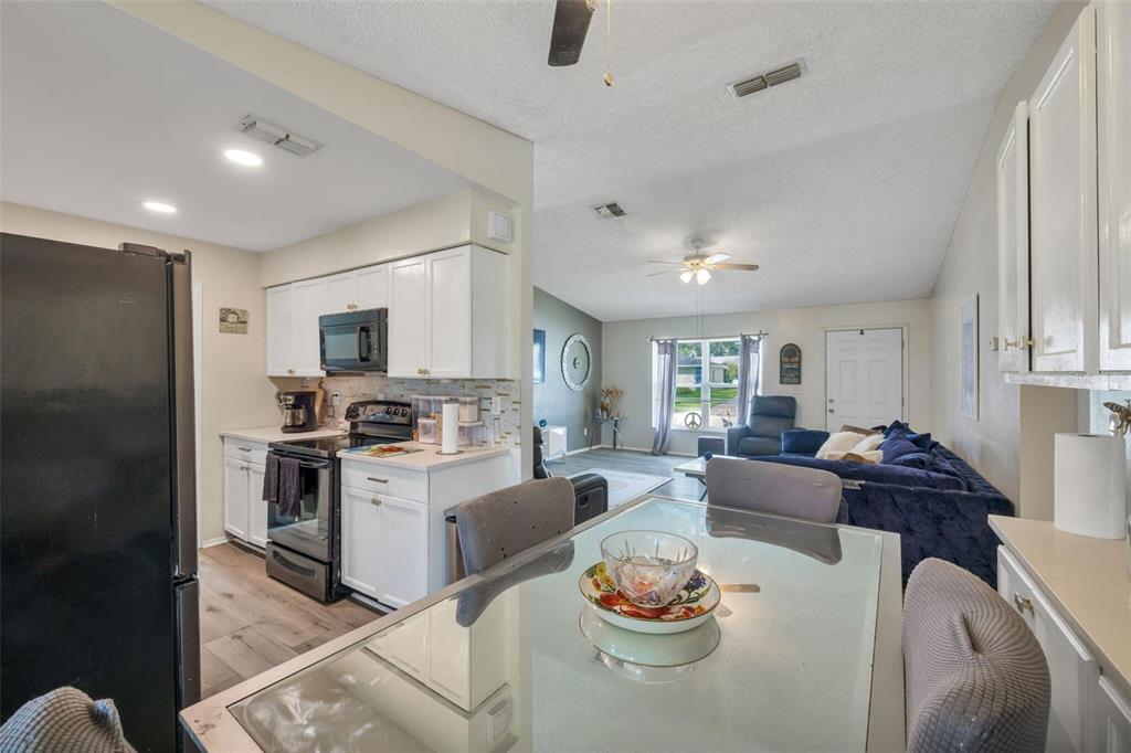 A kitchen with white cabinets and black appliances opens into a living room with blue furniture — 3900 105TH AVENUE N, CLEARWATER, FL
