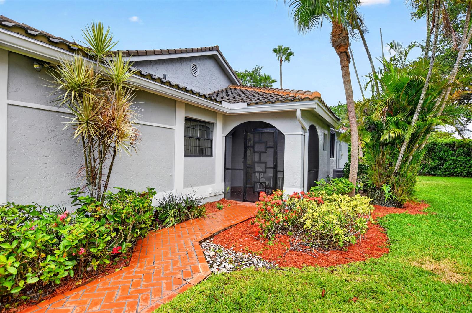 A brick walkway leads to a screened entryway of a house with gray stucco walls — 10523 Ladypalm # B, Boca Raton FL 33498, BOCA RATON, FL