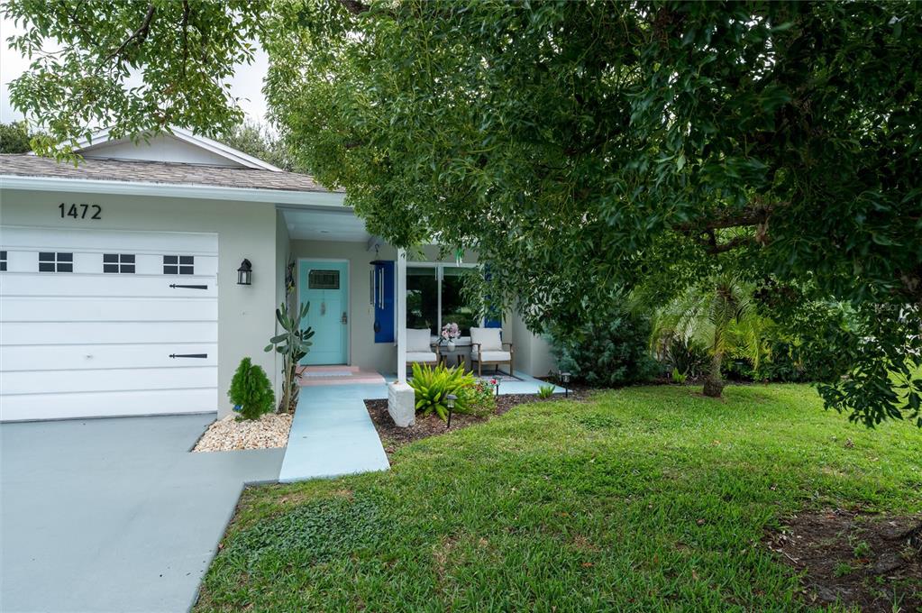 The exterior of a single-story house features a light-colored facade, a turquoise door, and a driveway — 1472 QUEEN ANNE DRIVE, PALM HARBOR, FL