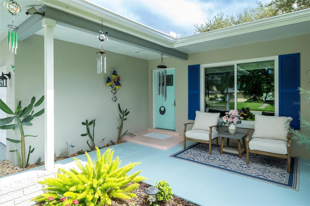 A covered front porch features a light blue floor, two chairs, and a turquoise door — 1472 QUEEN ANNE DRIVE, PALM HARBOR, FL