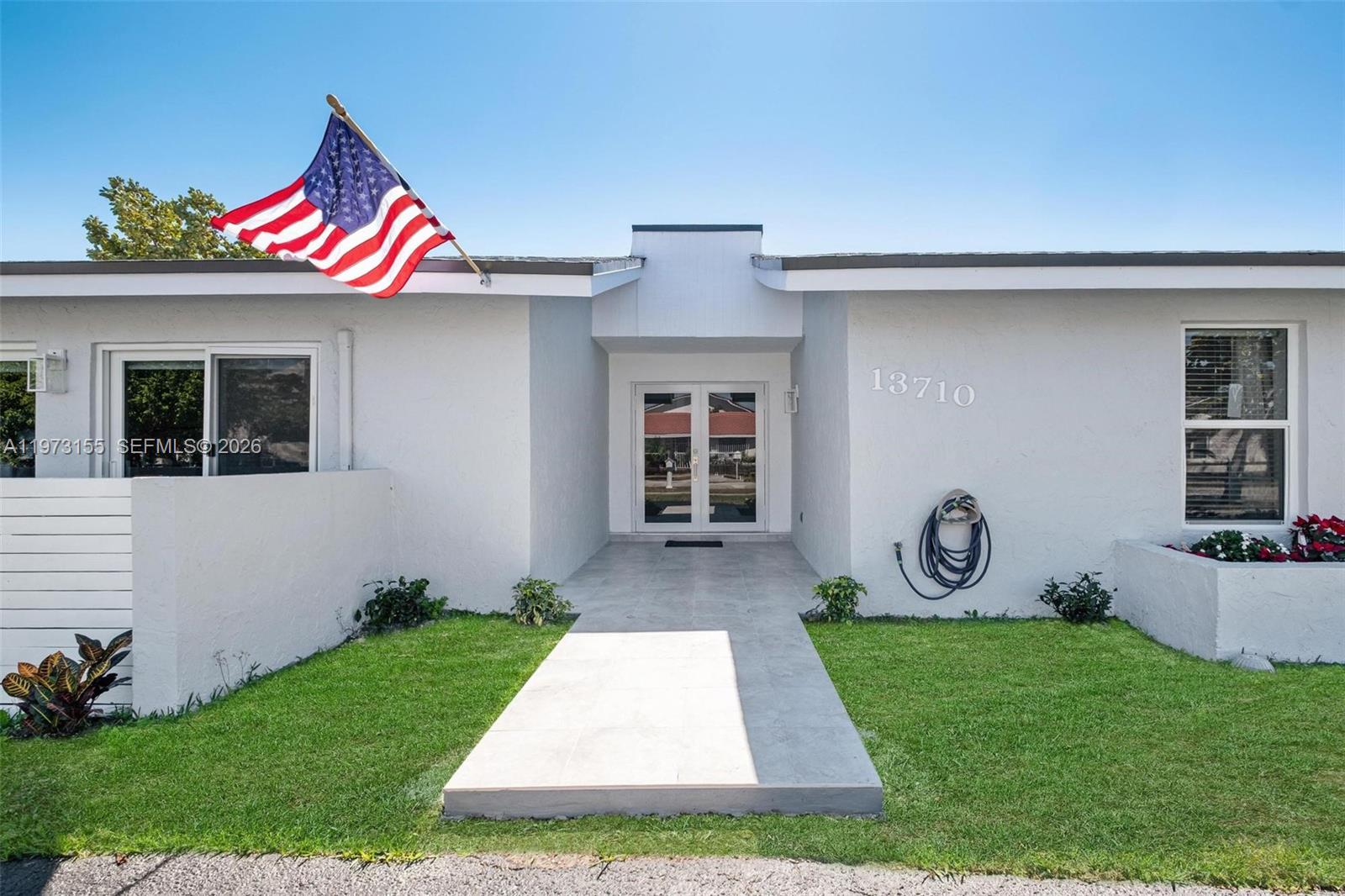 The exterior of a white house features a front walkway, double doors, and an American flag — 13710 SW 18th Ter, Miami FL 33175, MIAMI, FL
