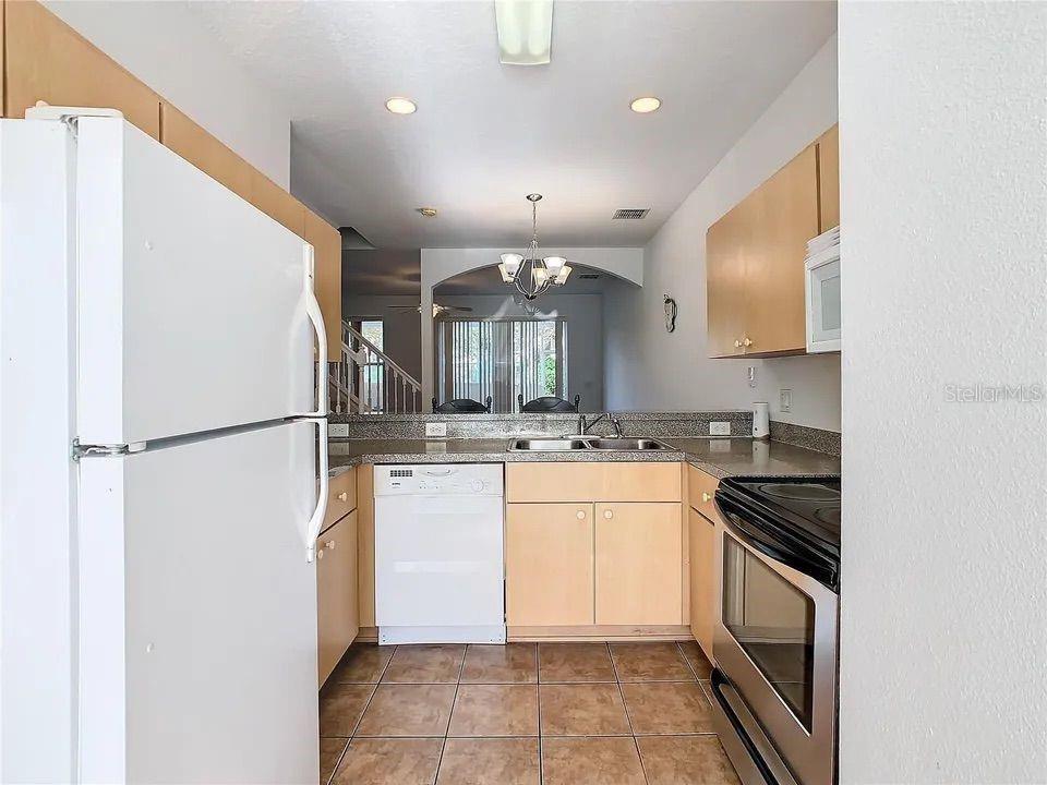 A kitchen features light wood cabinets, stainless steel appliances, and a view into the dining area — 4715 HEMINGWAY HOUSE STREET, KISSIMMEE, FL