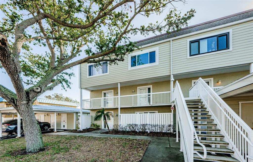 Exterior view of a multi-story apartment building with a staircase, balcony, and large tree — 433 S PAULA DRIVE UNIT 17, DUNEDIN, FL