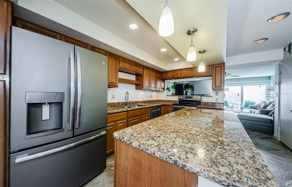 A kitchen features a large granite island, stainless steel refrigerator, and wood cabinetry — 433 S PAULA DRIVE UNIT 17, DUNEDIN, FL