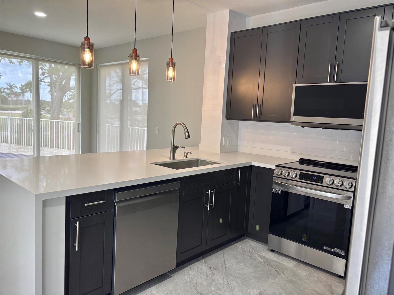 A modern kitchen features dark cabinetry, stainless steel appliances, white countertops, and three pendant lights — 17699 Tiffany Trace Drive, Boca Raton FL 33487, BOCA RATON, FL