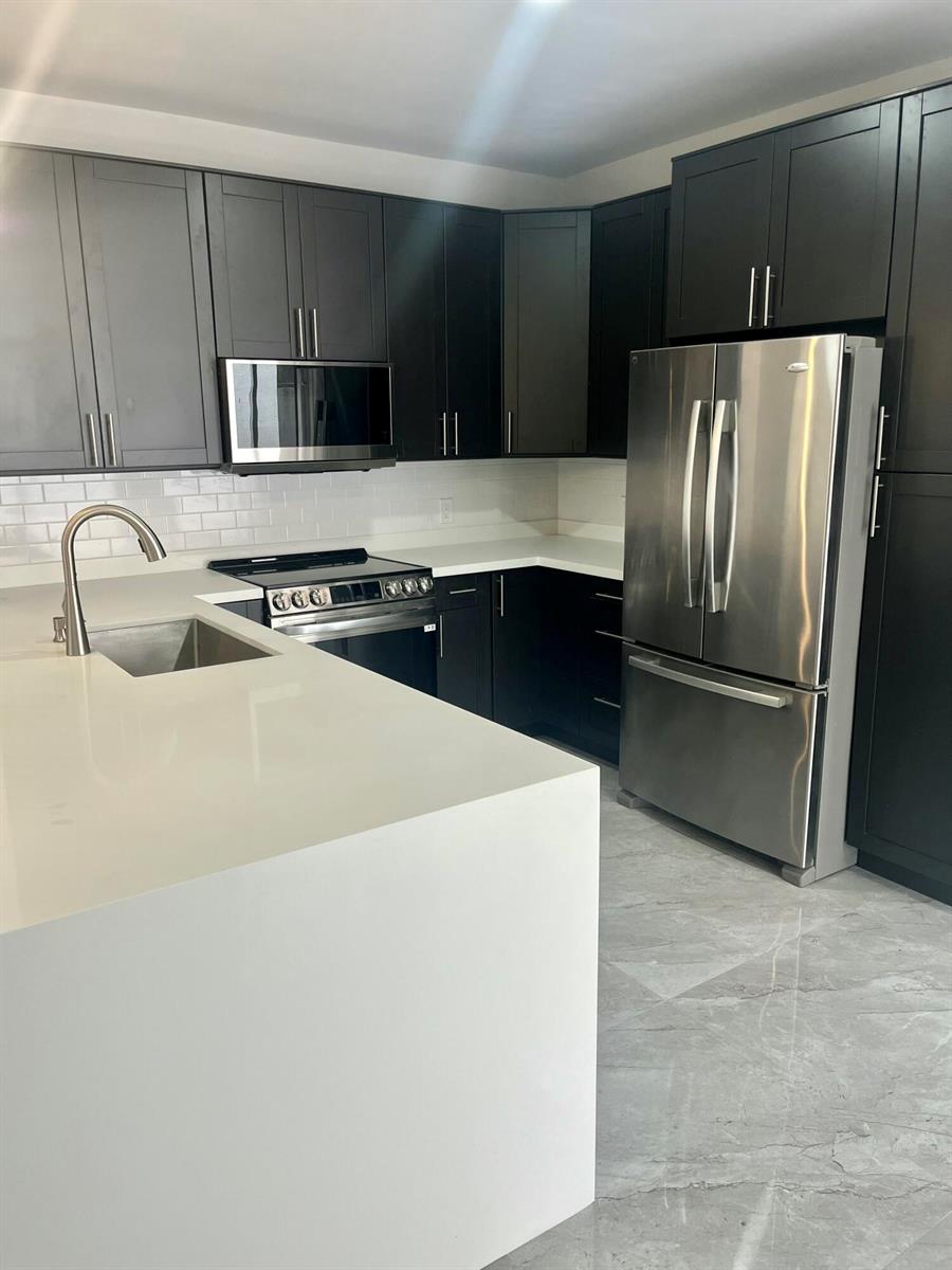 A modern kitchen features dark cabinetry, stainless steel appliances, white countertops, and gray tile flooring — 17699 Tiffany Trace Drive, Boca Raton FL 33487, BOCA RATON, FL