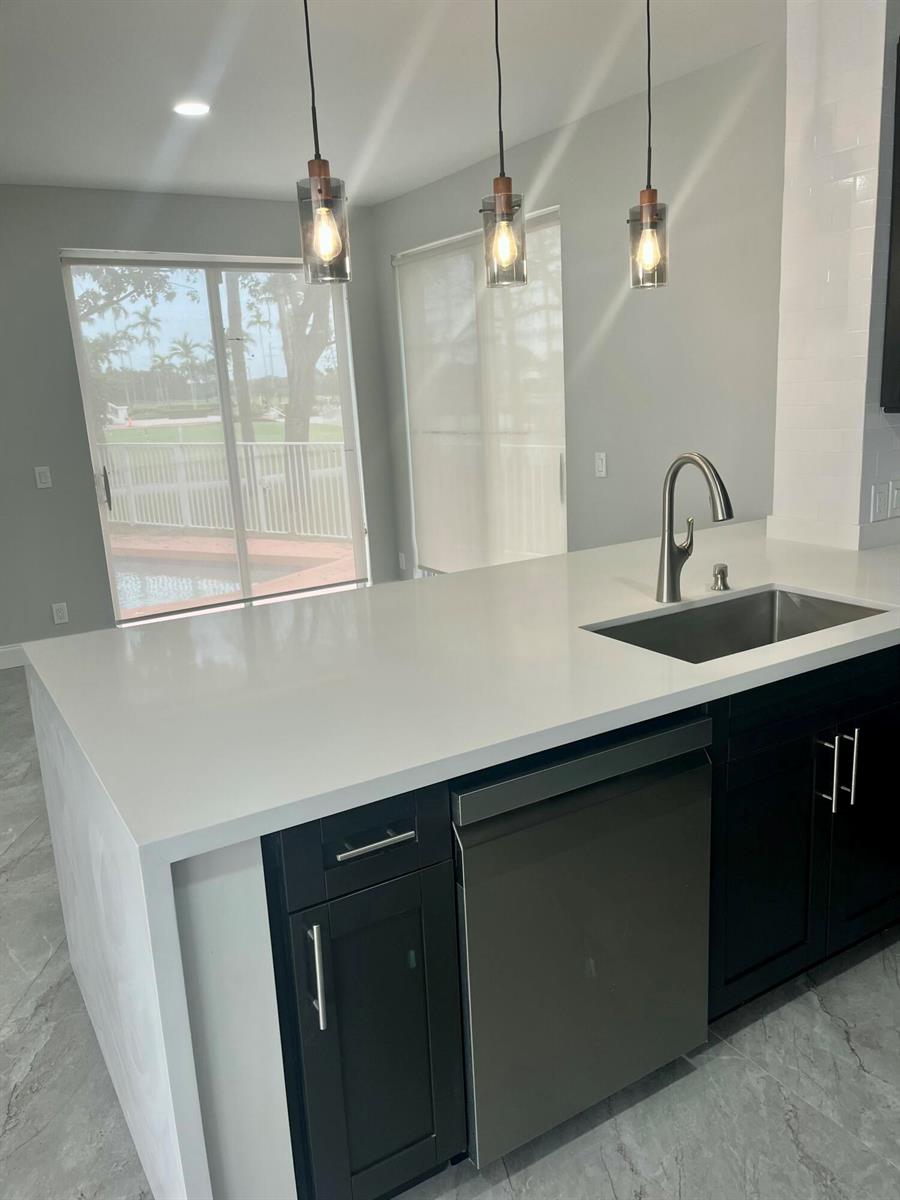 A modern kitchen island with a stainless steel sink and dishwasher faces a sliding door — 17699 Tiffany Trace Drive, Boca Raton FL 33487, BOCA RATON, FL