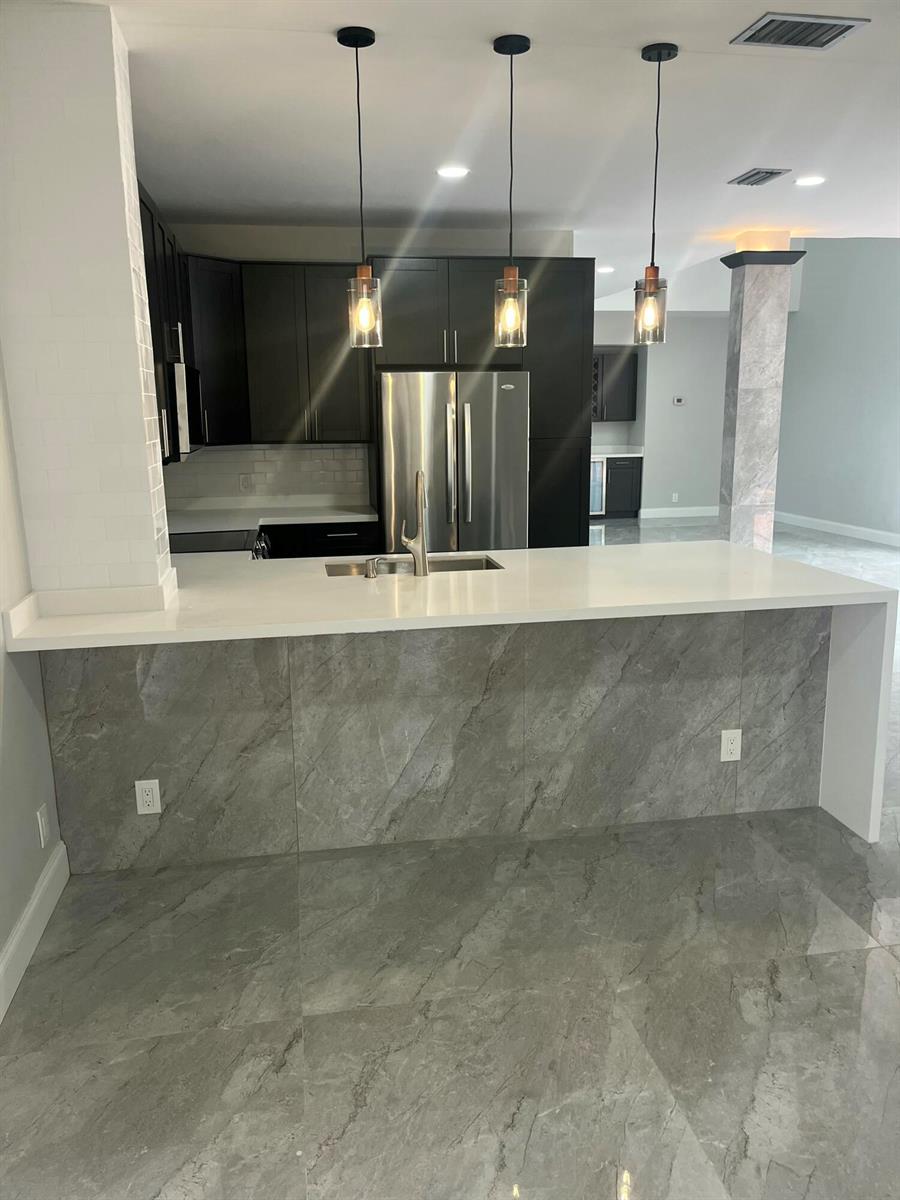 A kitchen island with a white countertop and gray marble-look base faces dark cabinets — 17699 Tiffany Trace Drive, Boca Raton FL 33487, BOCA RATON, FL