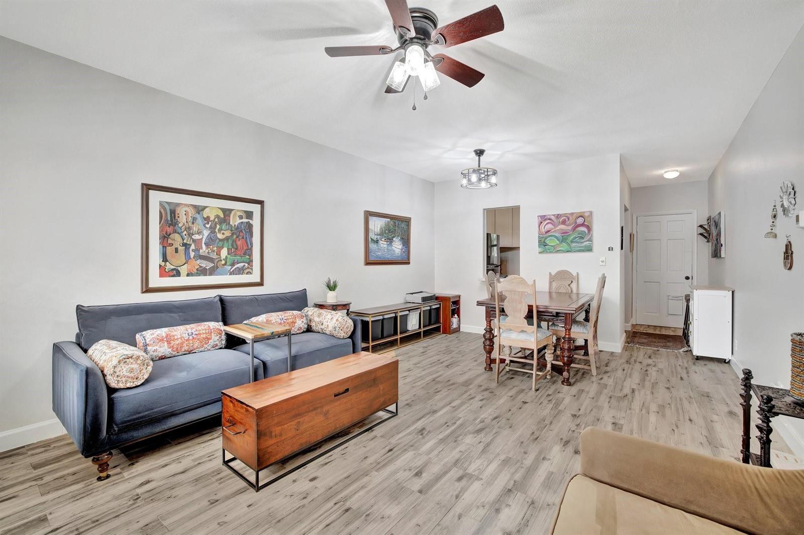 A living and dining area with gray wood-look flooring, a blue sofa, and a ceiling fan — 1450 N Riverside Drive # 102, Pompano Beach FL 33062, POMPANO BEACH, FL