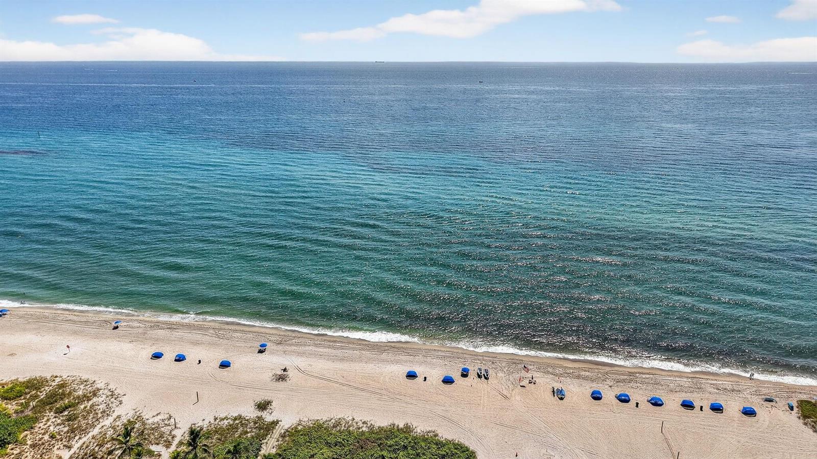 An aerial view shows a sandy beach with blue umbrellas along the ocean shoreline — 1450 N Riverside Drive # 102, Pompano Beach FL 33062, POMPANO BEACH, FL