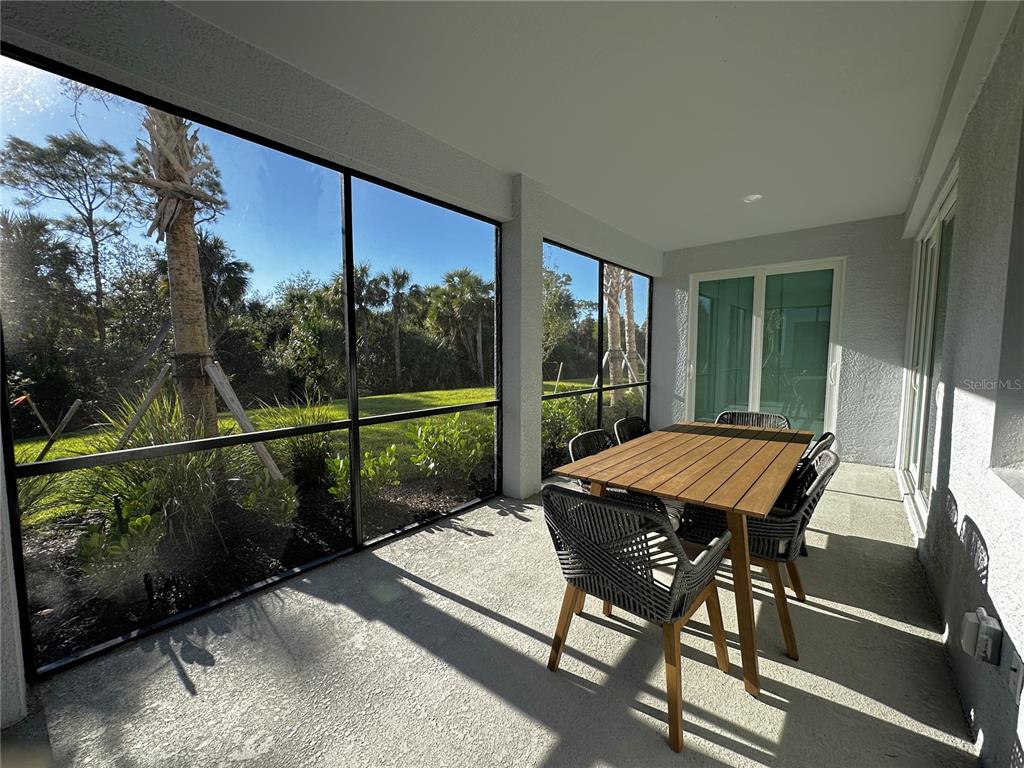 A covered patio with a dining set, screened walls, and a view of trees — 14161 POPPY FIELD LOOP UNIT 5811, PUNTA GORDA, FL