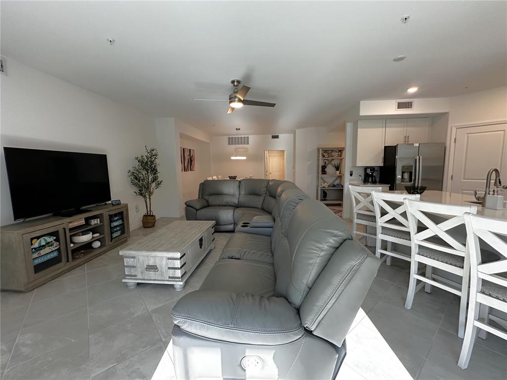 A living room with a gray sectional sofa, coffee table, and television faces an open kitchen — 14161 POPPY FIELD LOOP UNIT 5811, PUNTA GORDA, FL