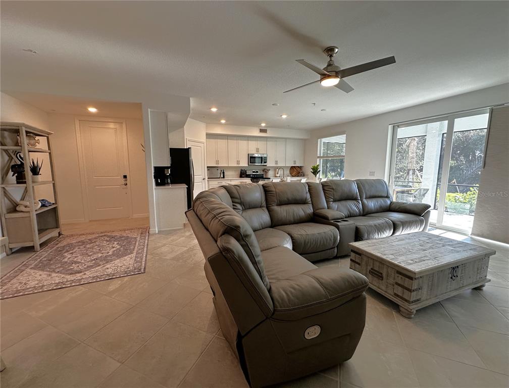 An open-concept living room features a large gray sectional sofa, tile flooring, and a kitchen — 14161 POPPY FIELD LOOP UNIT 5811, PUNTA GORDA, FL