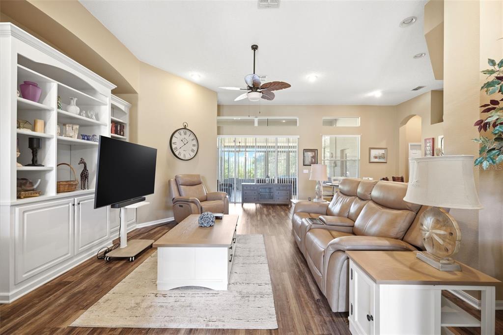 A living room features a television on a stand, a leather sofa, and wood flooring — 11407 LEEDS DRIVE, SPRING HILL, FL