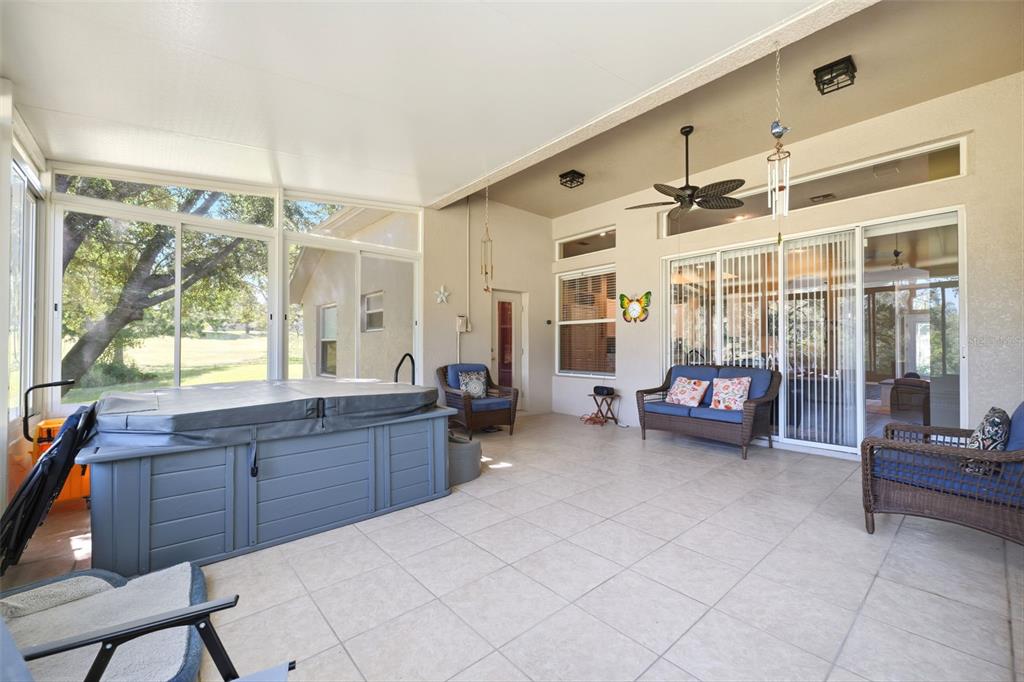 A covered patio features a hot tub, wicker furniture, tile flooring, and large sliding glass doors — 11407 LEEDS DRIVE, SPRING HILL, FL