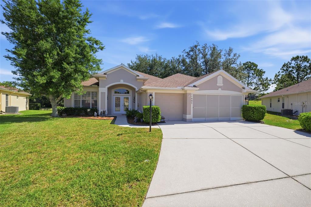 A single-story suburban house with a beige exterior, a two-car garage, and a concrete driveway — 11407 LEEDS DRIVE, SPRING HILL, FL