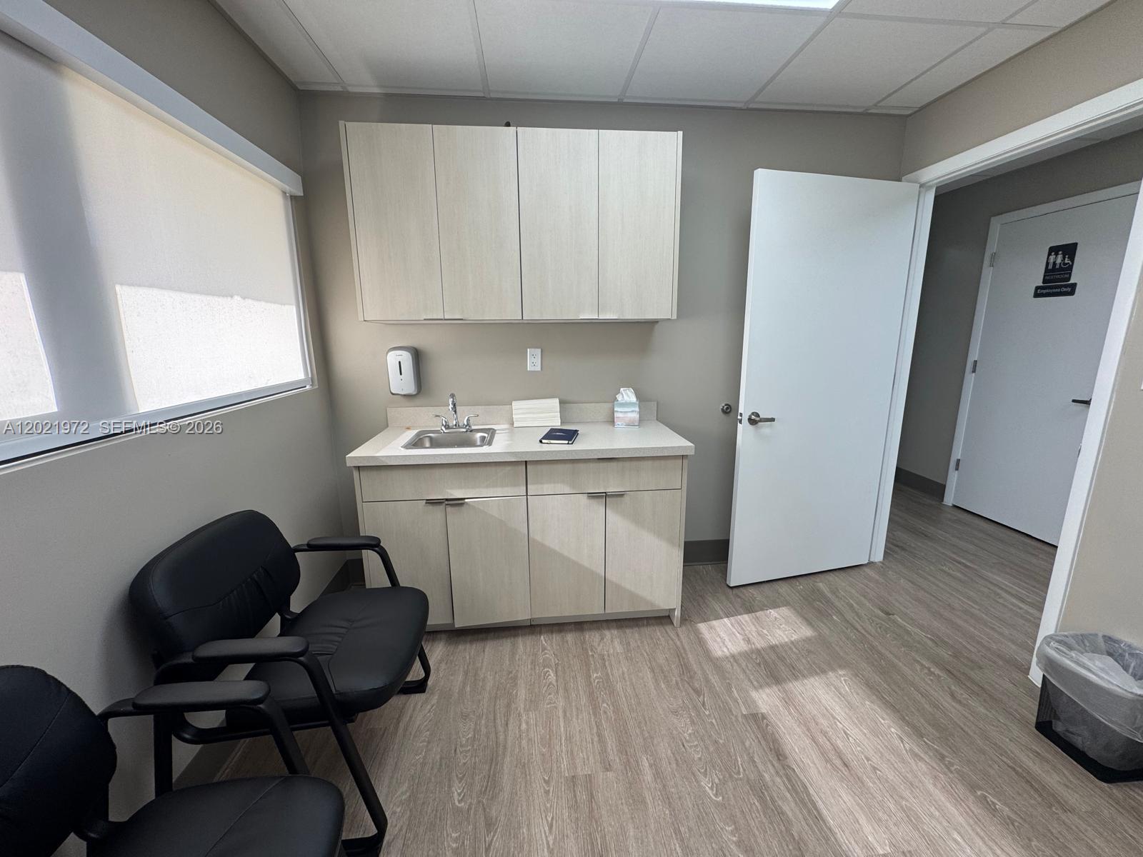 A medical exam room features light wood cabinetry, a sink, two black chairs, and flooring — 7100 W 20th Ave # 214, Hialeah FL 33016, HIALEAH, FL