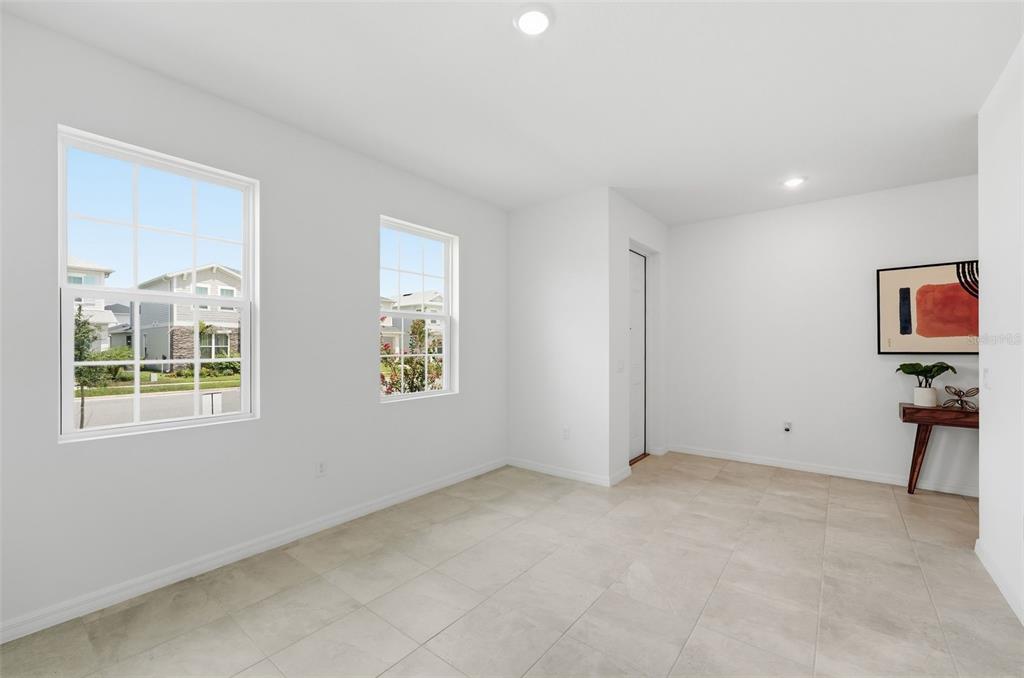 A bright, empty room features white walls, tile flooring, two windows, and a small console table — 1981 EDUCATION STREET, ST CLOUD, FL
