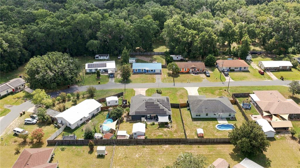 An aerial view shows several single-family homes with yards, swimming pools, and solar panels — 10544 SE 54TH AVENUE, BELLEVIEW, FL