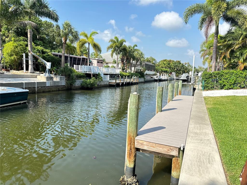 A wooden dock extends into a canal lined with palm trees and residential properties — 1723 STANFORD LANE, SARASOTA, FL