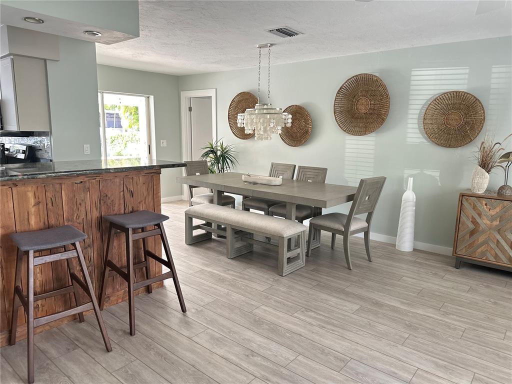 A dining room features a wooden table with chairs and a bench, plus wall-mounted wicker decor — 1723 STANFORD LANE, SARASOTA, FL