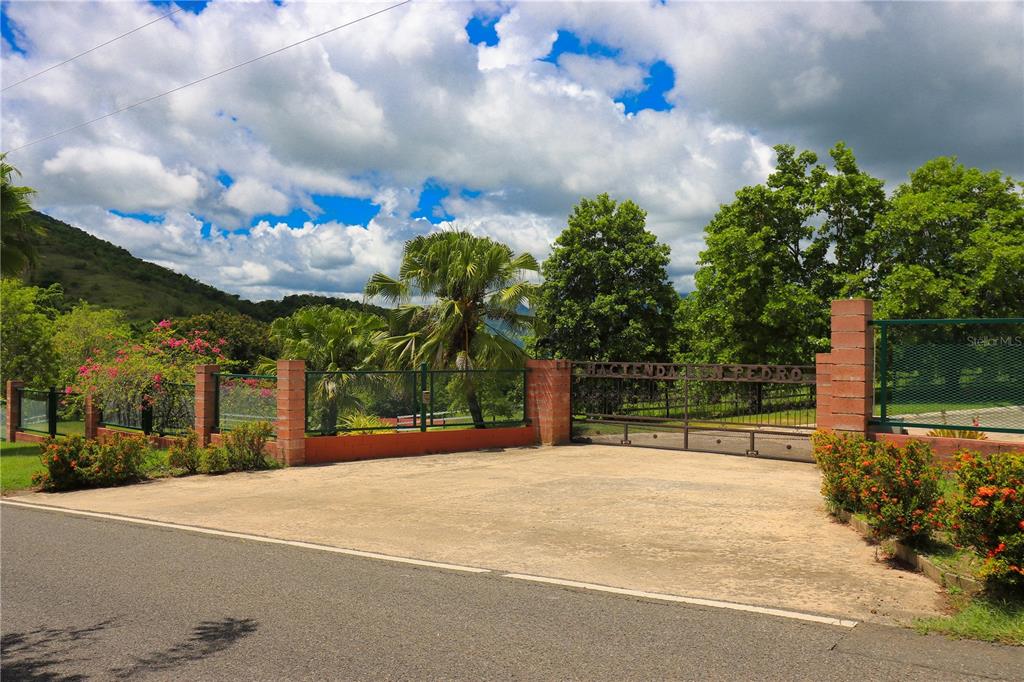 A paved driveway leads to a gated entrance with brick pillars and lush green landscaping — 150 CARR UNIT 10.8km, VILLALBA, PR