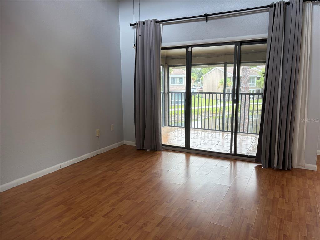 An empty room with wood-look flooring and sliding glass doors leading to a screened balcony — 5926 PEREGRINE AVENUE UNIT A13, ORLANDO, FL