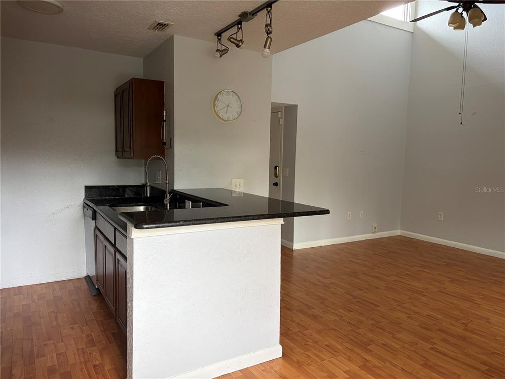 A kitchen with dark cabinets and a breakfast bar overlooks a living area with flooring — 5926 PEREGRINE AVENUE UNIT A13, ORLANDO, FL