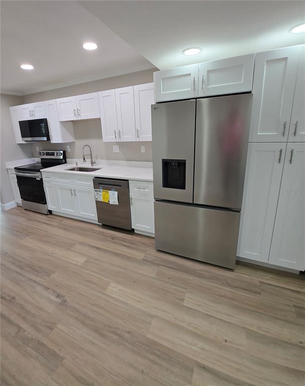 A kitchen features white cabinets, stainless steel appliances, and light wood-look flooring — 37406 VISTA DRIVE, DADE CITY, FL